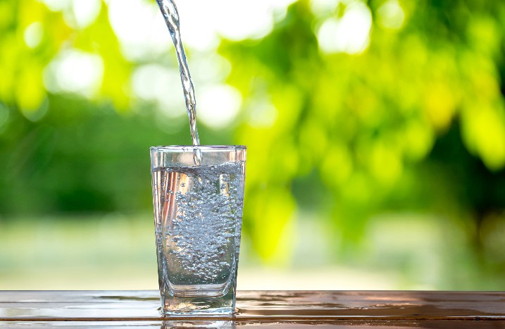 Wasser wird in ein Glas auf Gartentisch gefüllt.